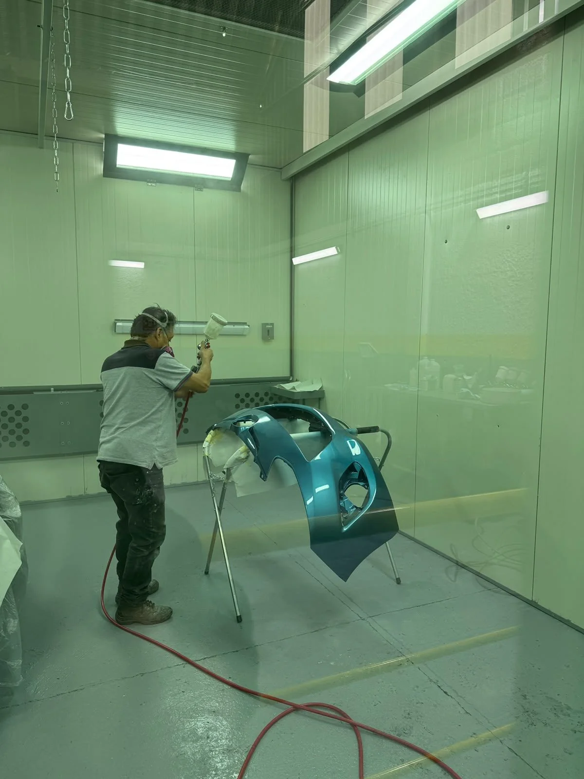 Técnico de Tlahuiauto aplicando pintura a una defensa dentro de la cabina
